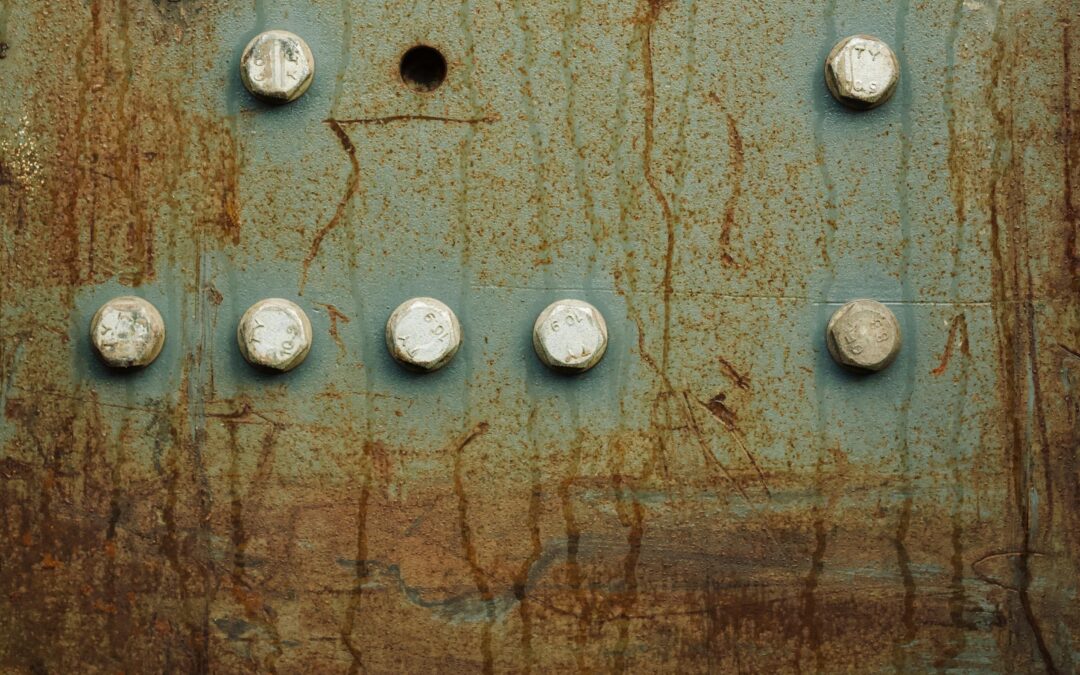 Close-up of a rusted metal panel featuring a row of hex bolts and a central circular hole, with brown streaks and weathered blue-green paint.